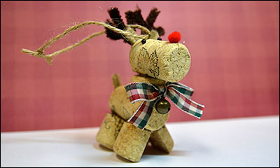 bottle cork reindeer ornament with red cottonball nose, pipe cleaner antlers, and red, while, and green tartan bow with bell
